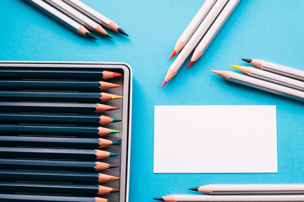 Colorful pencils in box with blank paper card on blue desk.