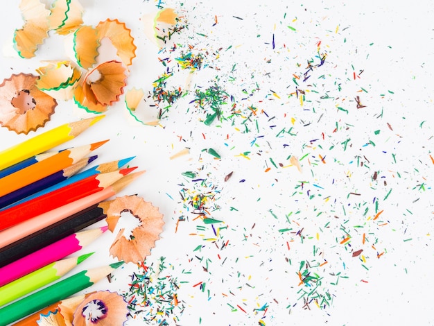 Colorful pencils with colorful pencil shavings on white background