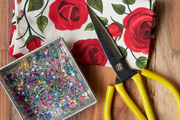 Colorful pins in metal tray There are yellow scissors and cloth placed on the sides.