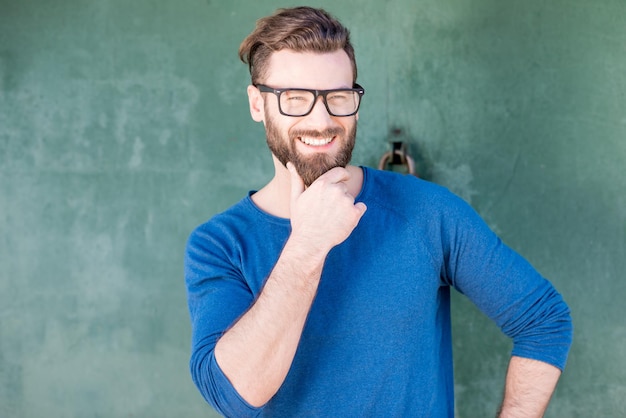 Colorful portrait of a handsome man dressed in blue sweater standing on the green rusty wall background