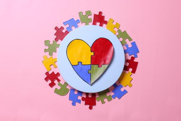 Colorful puzzle heart shape on white plate surrounded by colorful puzzles on pink background