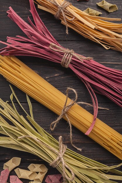 Colorful raw purple beetroot, green spinach and classical yellow pasta on dark wooden background. Creative meal, Italian cuisine concept, closeup