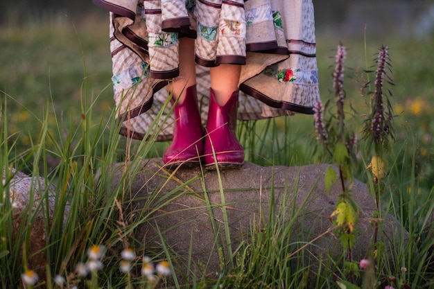 Colorful  red rain boots on woman feet,  standing  on a rock in a meadow with flowers.