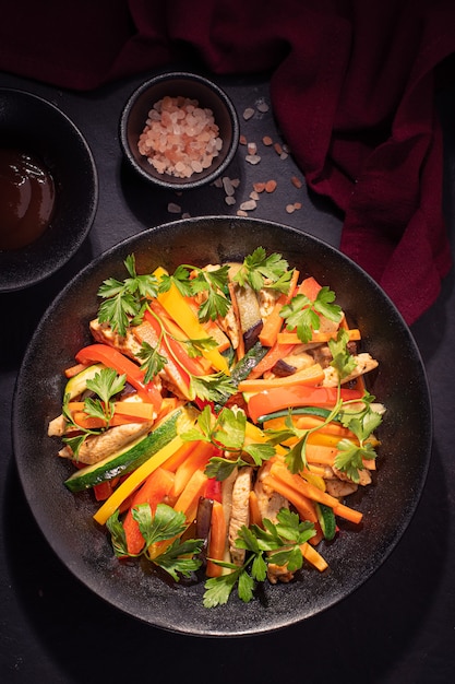 Colorful salad with fried chicken and a slice of carrot and zucchini on black background.