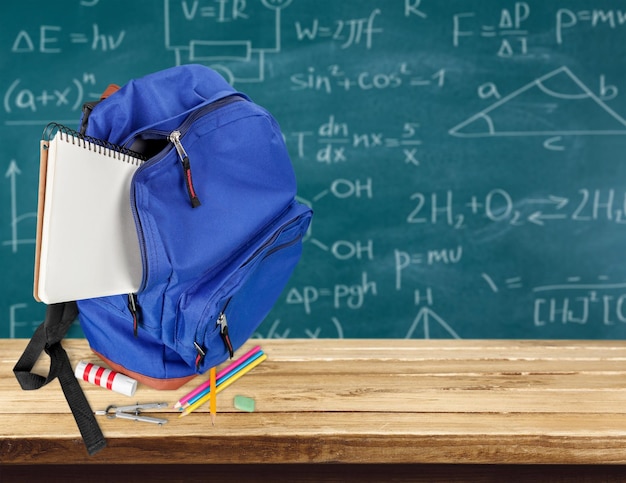 Colorful school supplies in backpack on wooden background