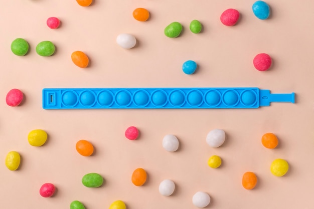 Colorful silicone toy antistress Pop It bracelet on a background with multicolored candies