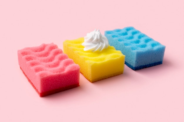 Colorful sponges for dishwashing with foam on pink background. Cleaning service concept