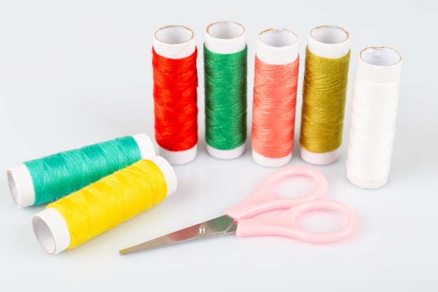 Colorful spool of threads and scissors on white background