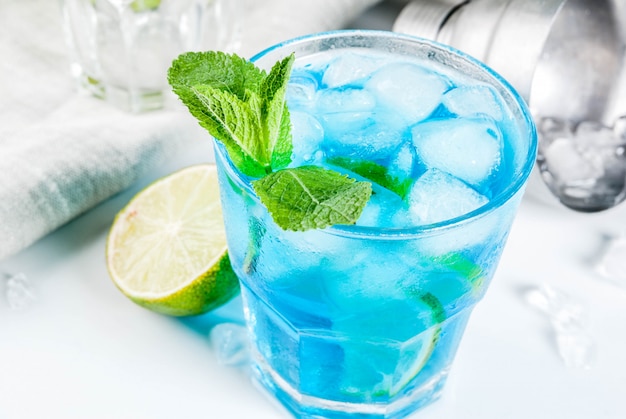 Colorful summer beverage, iced blue lagoon alcohol cocktail drink with lime and mint 