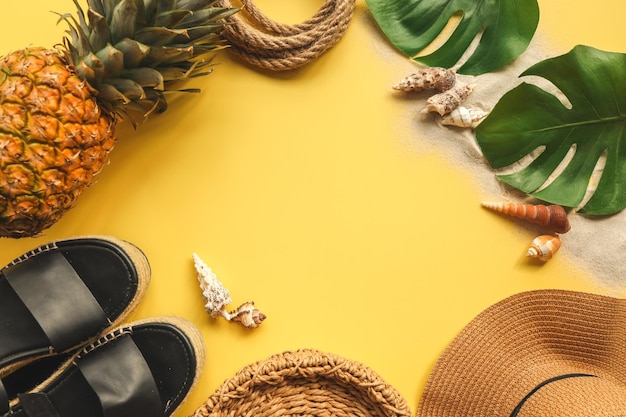 Colorful summer female fashion outfit flat lay Straw hat wicker shoes pineapple over yellow background top view wide composition Summer fashion holiday concept