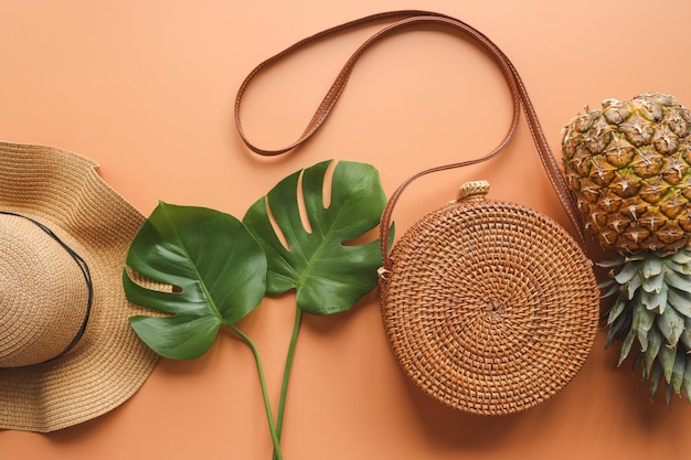 Colorful summer female fashion outfit flatlay Straw hat bamboo bag palm branches pineapple over beige background top view wide composition Summer fashion holiday concept