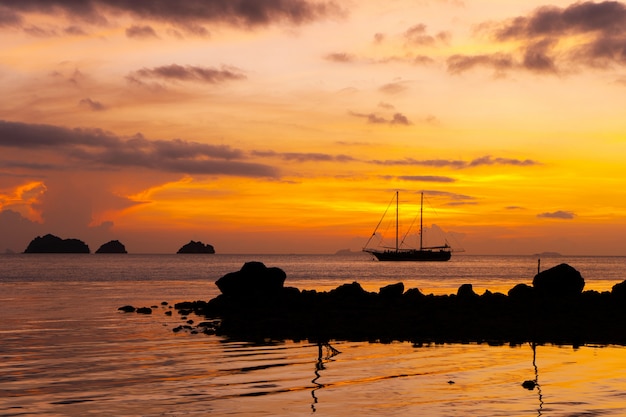 Colorful sunset on a tropical beach. Orange sunset on the ocean. Colorful sunset in the tropics. In the water is a sailing ship. Silhouetted sailboat with masts