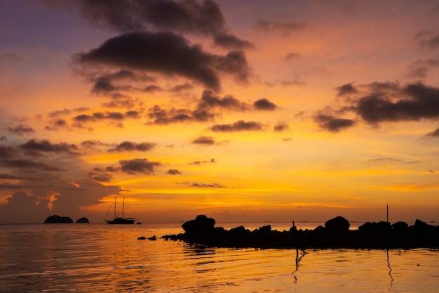 Colorful sunset on a tropical beach. Orange sunset on the ocean. Colorful sunset in the tropics. In the water is a sailing ship. Silhouetted sailboat with masts