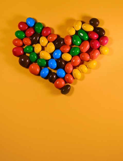 Colorful sweet candies are laid out in the shape of a heart Yellow background