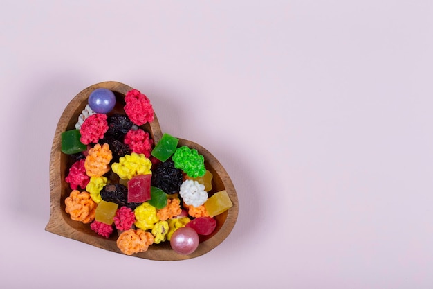 Colorful sweets and candies are poured into a heartshaped wooden vase