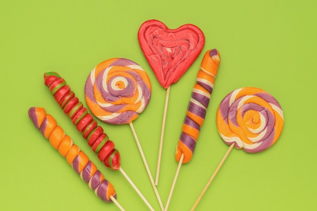 Colorful sweets on sticks on a green background Minimal concept of sweet life and love