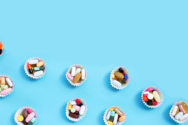 Colorful tablets with capsules and pills in cupcake wrappers on blue background.