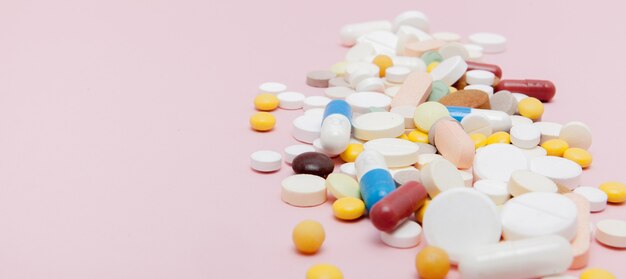 Colorful tablets with capsules on a pink background.