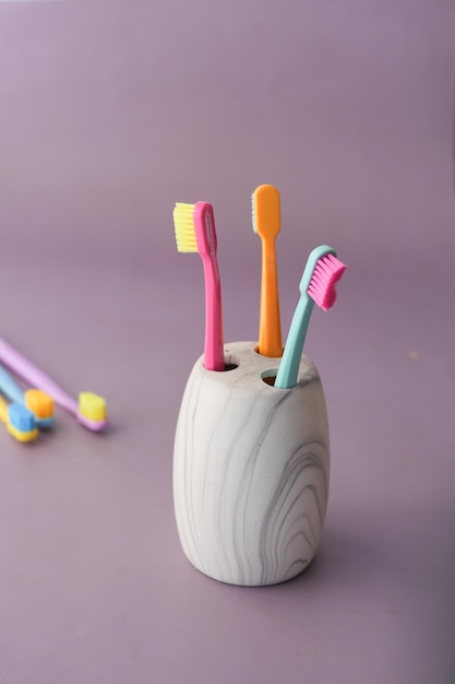 Colorful toothbrushes in white mug on purple background