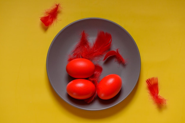 Colorful traditional painted Easter eggs. Red eggs, yellow background. Three eggs in a gray plate