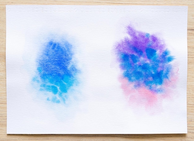 Colorful watercolor brush strokes on white paper sheet with wood background Closeup