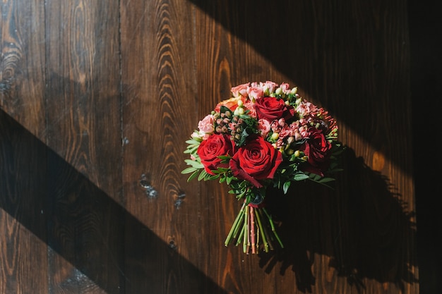 colorful wedding bouquet on table made of dark wood in rays of bright sun red and pink roses