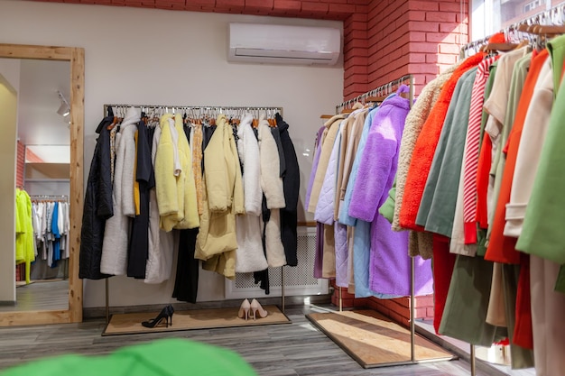 Colorful women's dresses, jackets, trousers and other clothes on hangers in a retail store.