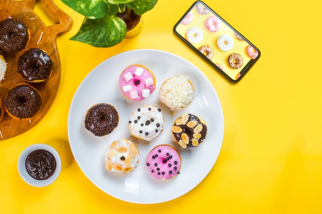 Colourful doughnuts served on a white plate on yellow background