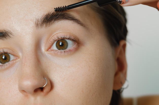 Combing her eyebrows with a brush in a beauty salon. Woman with long eyelashes and thick eyebrows.