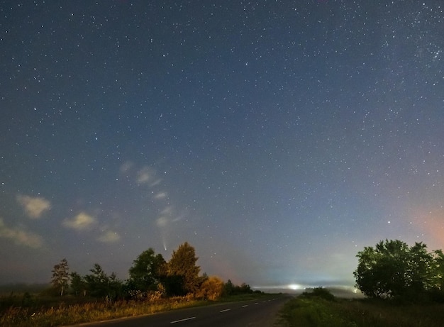 Comet Neowise C2020 F3 as it flies overhead in the summer sky over over meadow near countryside road Lviv Region Ukraine