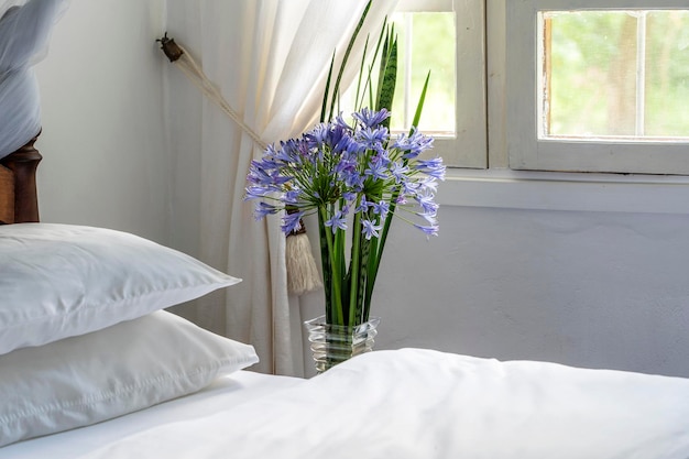 Comfortable soft bed in room and a bouquet of flowers near the window close up