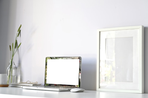 Comfortable workplace with blank screen laptop computer and mockup poster on white desk office table