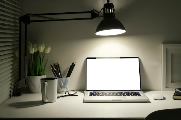 Comfortable workplace with laptop lamp flower pot and stationery on white table