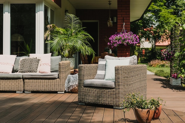 Comfy wicker armchair with pillows on wooden terrace of trendy suburban home