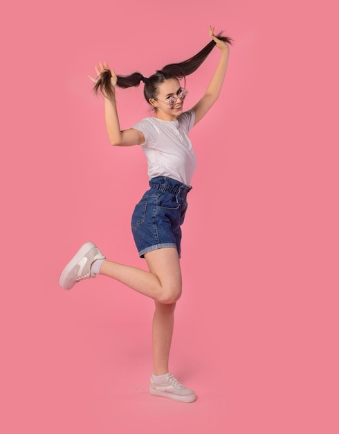 comic young girl wearing glasses fooling around jumping isolated on pink background