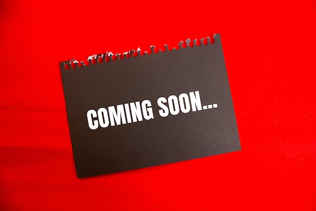 Photo coming soon message written on ripped black paper piece with red background conceptual coming soon symbol copy space