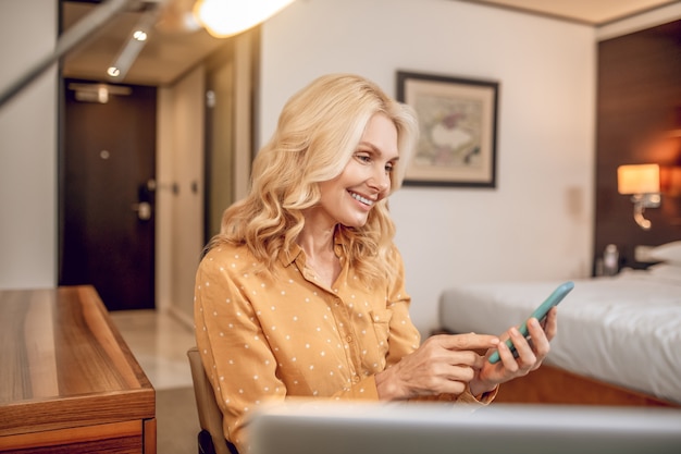 Communication. Blonde pretty woman sitting in an arm-chair with a phone in hands