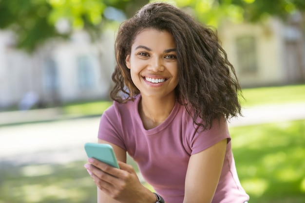 Communication. A cute girl in a pink tshirt spending time in the park and chatting online