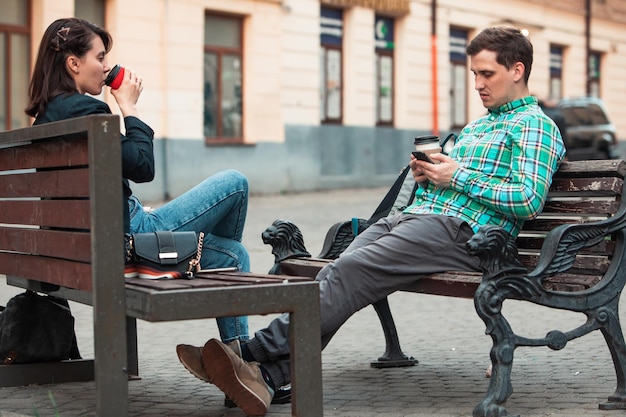 Communication problem man with woman sitting on bench at city street drinking coffee in paper cup looking ito phones lifestyle concept shy to speak