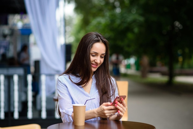 Communication technology and people concept happy smiling young woman with coffee and smartphone on city street