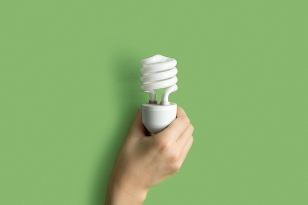 Photo compact fluorescent lamp lamp in human hand helical integrated cfl lightbulb on green pastel color background idea creativity concept flat lay design banner top view photo mockup lighting eco