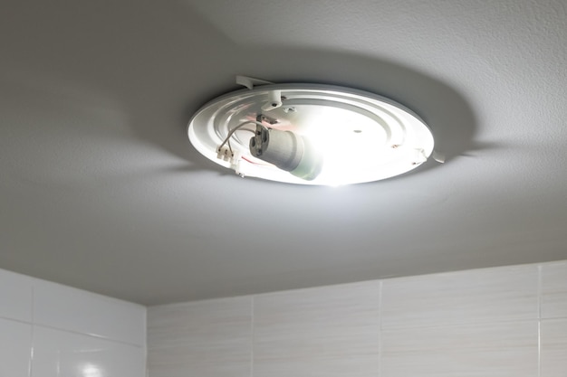 The compact LED bulb on the white ceiling of the bathroom in the urban house front view with the copy space