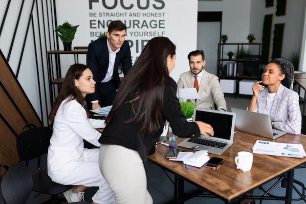 Company employees discussing during a meeting in the office at a large desktop with laptops and