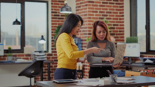 Company employees working together in business partnership, using laptop to brainstorm strategy ideas. Team of asian women analyzing information on device for financial success.