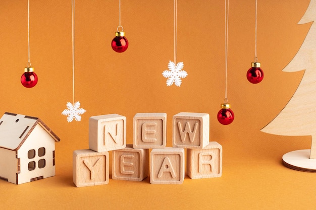 Composed the word new year from wooden cubes on an orange background Wooden house Christmas tree and other Christmas decorations Christmas card