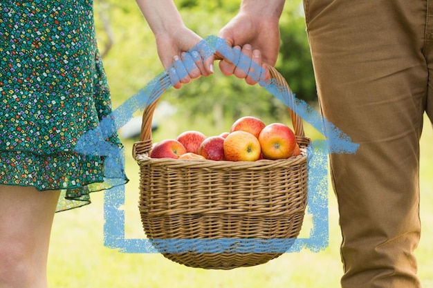 Composite image of basket of apples being carried by a young couple