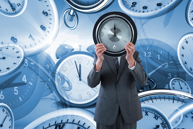 Composite image of businessman holding clock in front of his face