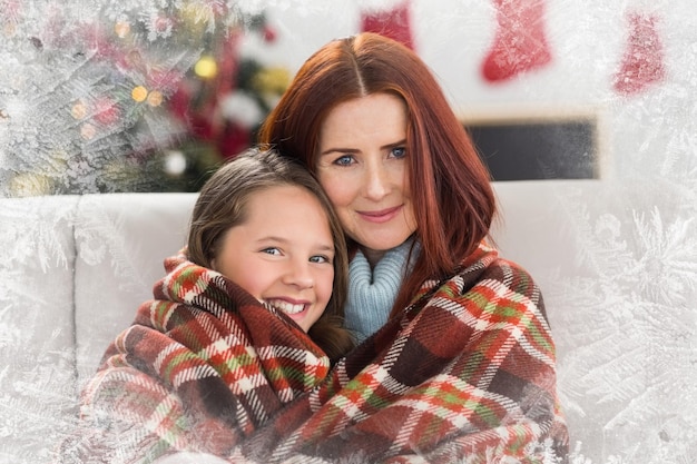 Composite image of festive mother and daughter wrapped in blanket