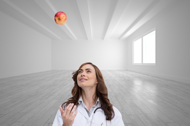 Composite image of happy doctor throwing apple