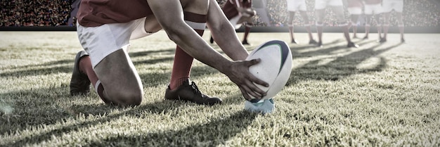 Composite image of male rugby player placing rugby ball on a stand in the rugby playground